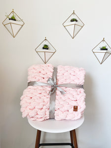 Pink chunky knit blanket folded and tied with a satin ribbon on a comfy chair
